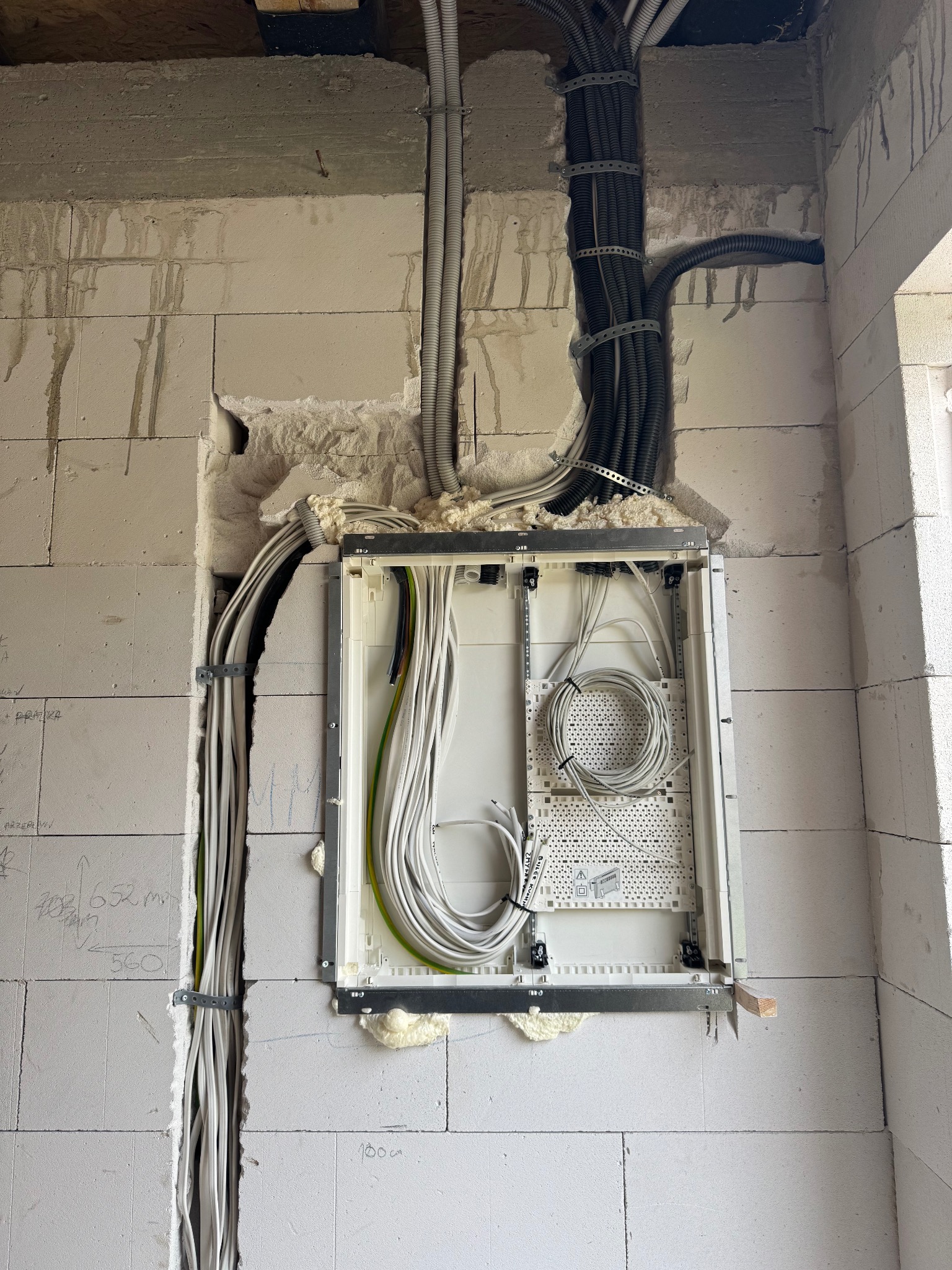 Wewnętrzna instalacja elektryczna w bloku z betonu komórkowego. Przewody w peszlach i korytkach, puszka rozdzielcza w ścianie. Etap prac przed tynkowaniem.