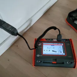 Miernik Sonel MPI-540-PV z podłączoną sondą w gniazdku elektrycznym, wyświetlający wynik pomiaru impedancji pętli zwarcia ZL-N, obok leży otwarty futerał na przyrządy.