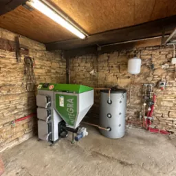 Nowoczesny piec grzewczy Integra z zbiornikiem buforowym w kotłowni o kamiennych ścianach, oświetlony jarzeniówką. Widoczne przyłącza hydrauliczne.