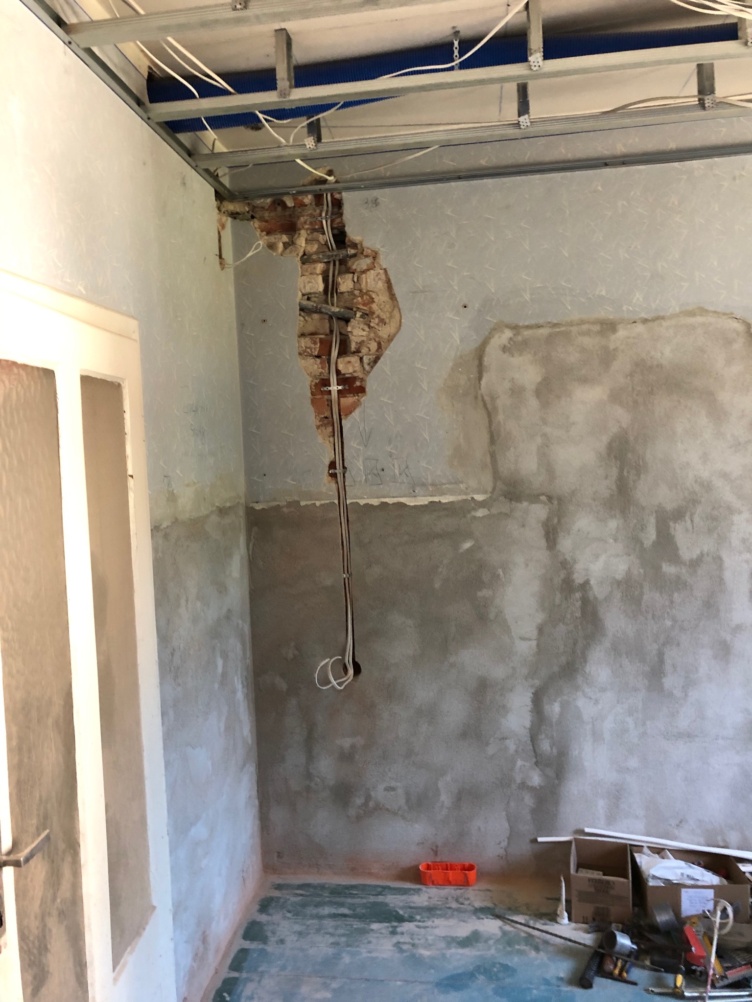 Przygotowanie do położenia sufitu podwieszanego: widoczne profile metalowe, odsłonięta cegła z przewodami elektrycznymi, fragment ściany z resztkami tapety i nałożoną gładzią, oraz narzędzia...