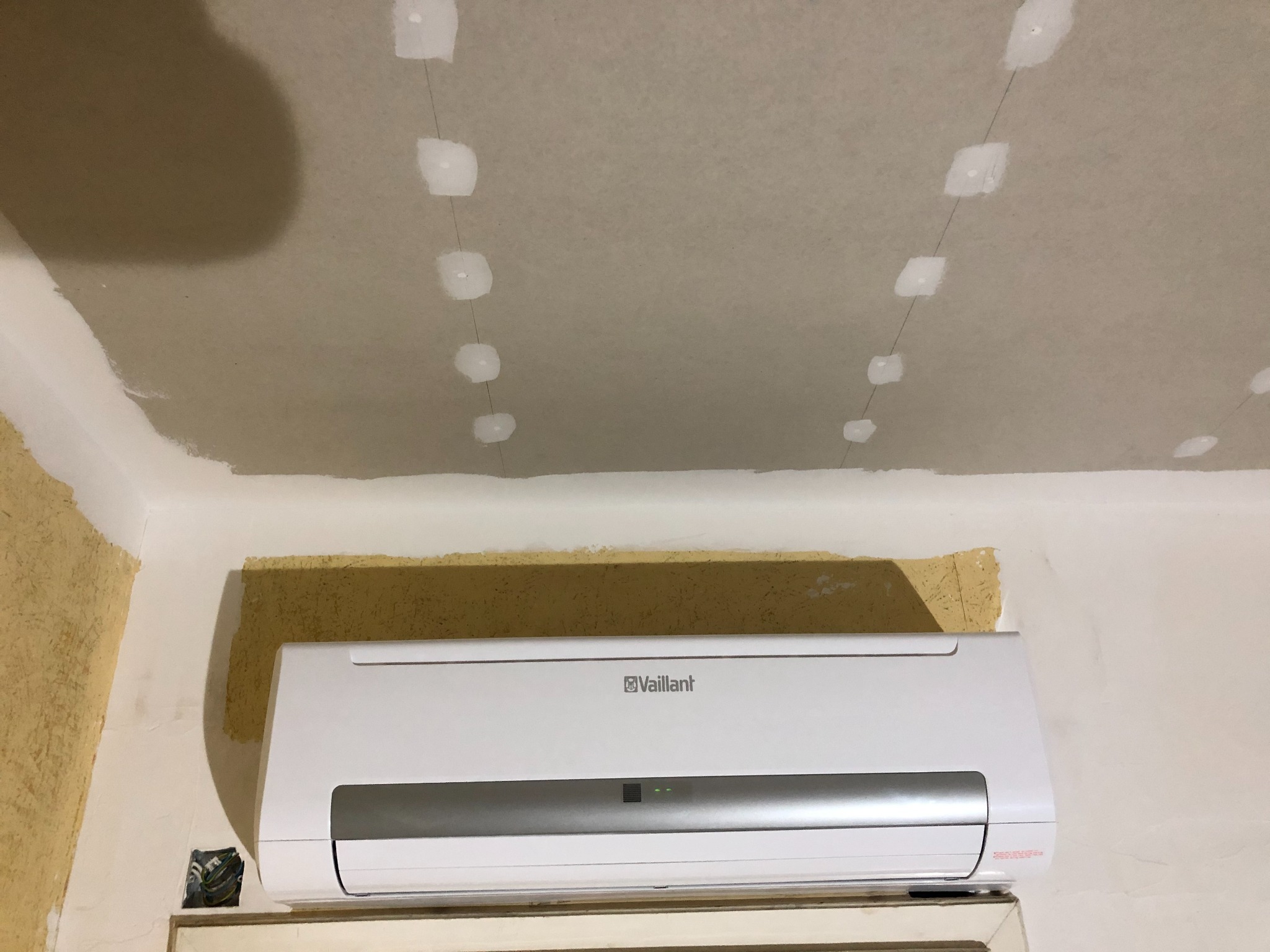 Przygotowanie sufitu pod napinanie, widoczne punkty mocowania i wiszące linki, zamontowany klimatyzator Vaillant na ścianie, ślady po starej tapecie.
