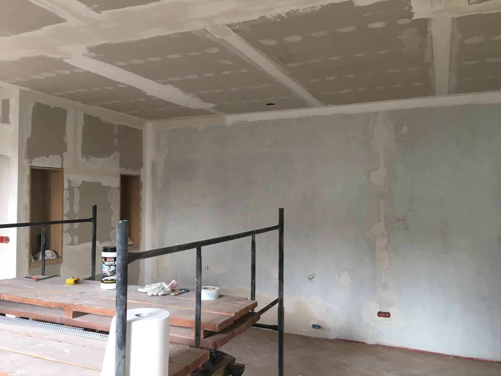 Wnętrze w trakcie prac przygotowawczych do malowania, widoczne rusztowanie, ściany z miejscowymi poprawkami, sufit z płyt gipsowo-kartonowych przed szpachlowaniem, rolka papieru i pojemnik...