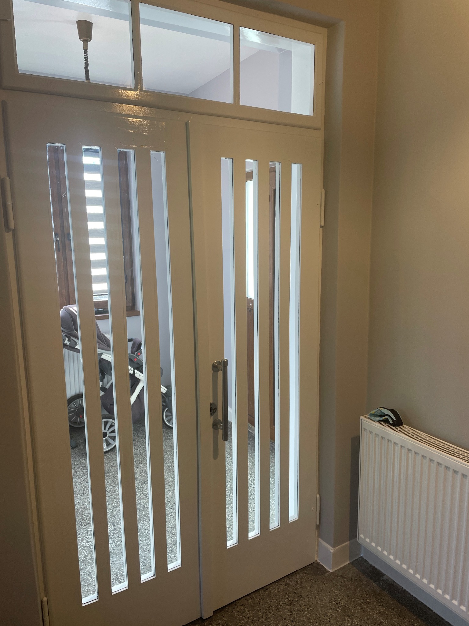 Białe, przeszklone drzwi wewnętrzne z pionowymi wstawkami, widoczne z perspektywy korytarza w Żywcu, z grzejnikiem i elementami wyposażenia wnętrza w tle.