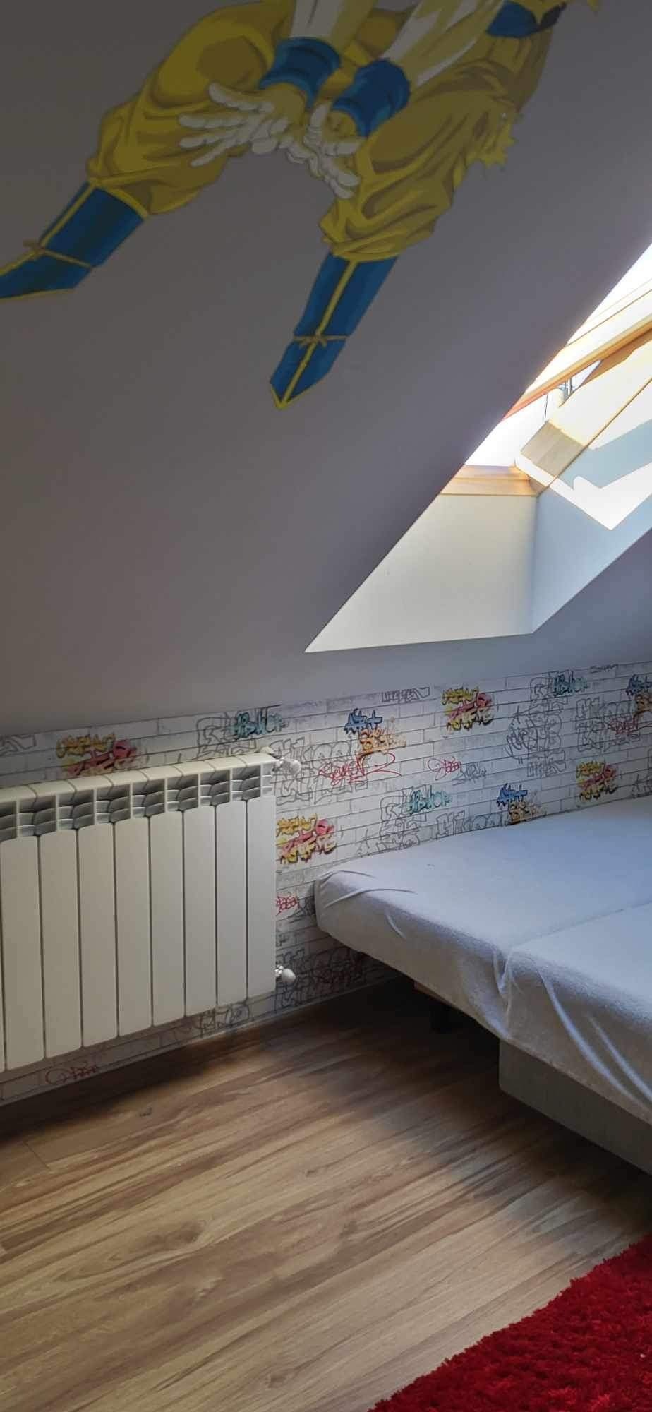Pokój na poddaszu z oknem dachowym, grzejnikiem aluminiowym, tapetą w graffiti i rysunkiem postaci z bajki na suficie.