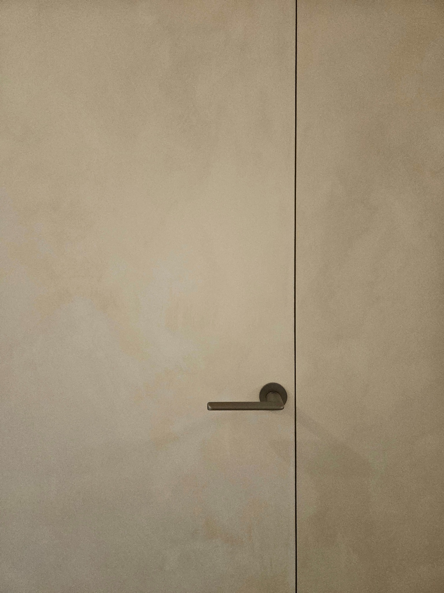 Beżowe drzwi z ukrytą ościeżnicą i klamką na tle ściany o delikatnej fakturze, wykończonej techniką lime wash.