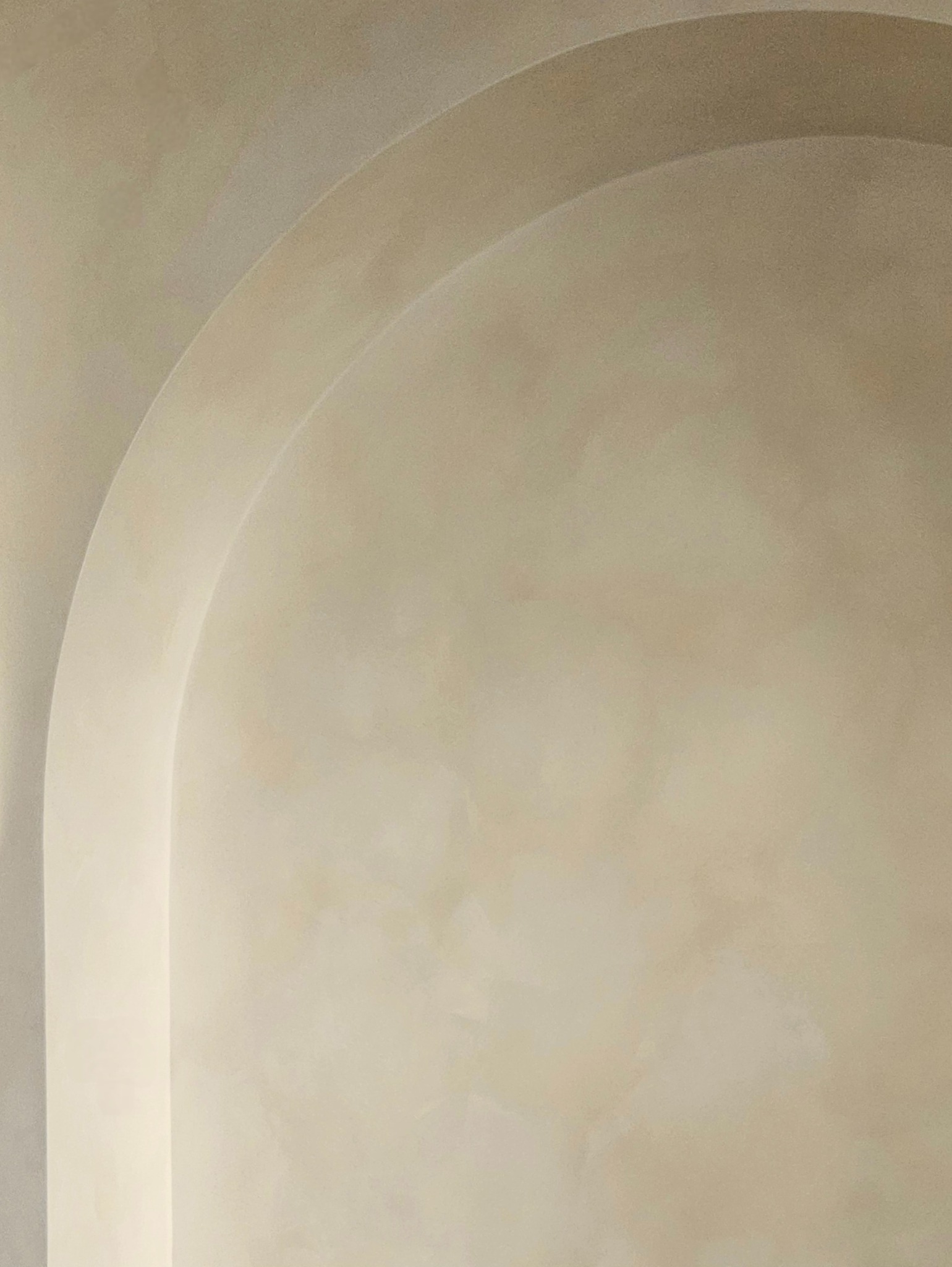 Beżowa ściana z dekoracyjnym efektem lime wash i subtelnymi, łukowatymi elementami architektonicznymi, tworzącymi minimalistyczną, ciepłą przestrzeń.