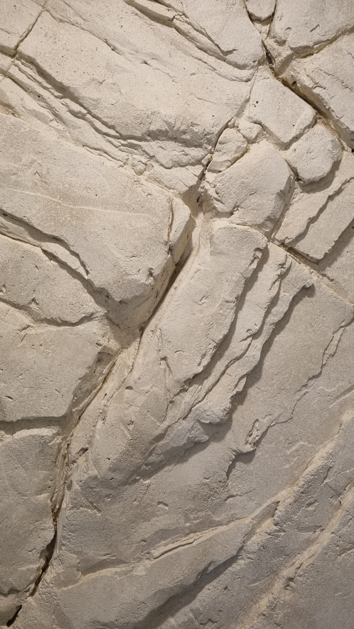 Jasna ściana z efektem skały, imitująca naturalny kamień. Wyraźna faktura, nieregularne kształty i delikatne cieniowanie. Dekoracyjna powierzchnia z mikrocementu.