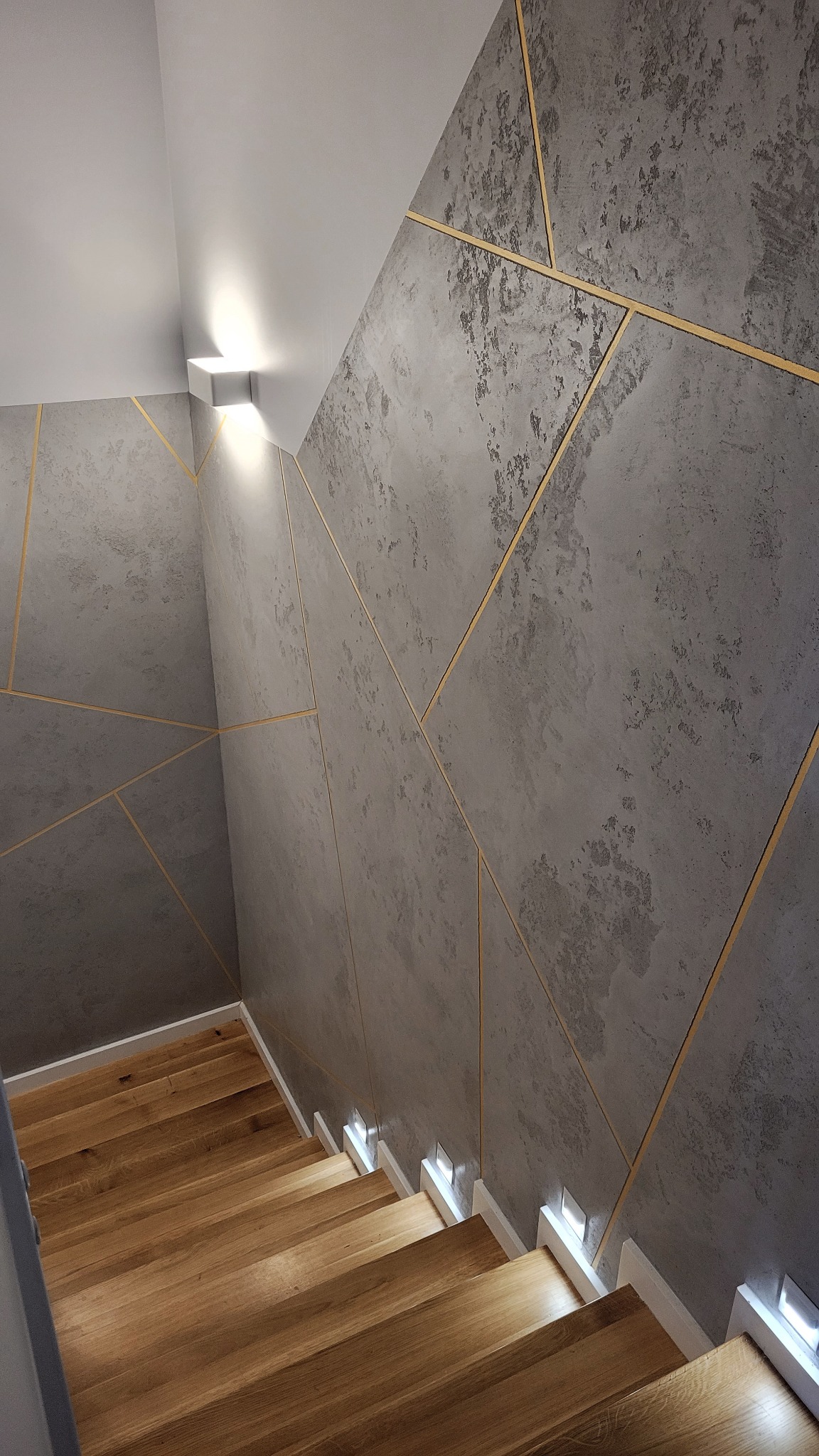 Beton architektoniczny z geometrycznym podziałem i złotą fugą zastosowany w klatce schodowej