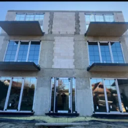 Surowy budynek z zamontowanymi oknami z białymi ramami i betonowymi balkonami, w trakcie budowy, widok z dołu na błękitne niebo.