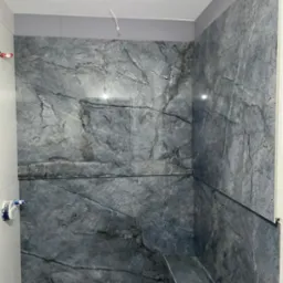 Ściana i półka w łazience wyłożone płytkami imitującymi szary marmur z wyraźnym użyleniem, widoczne wyprowadzone kable elektryczne.