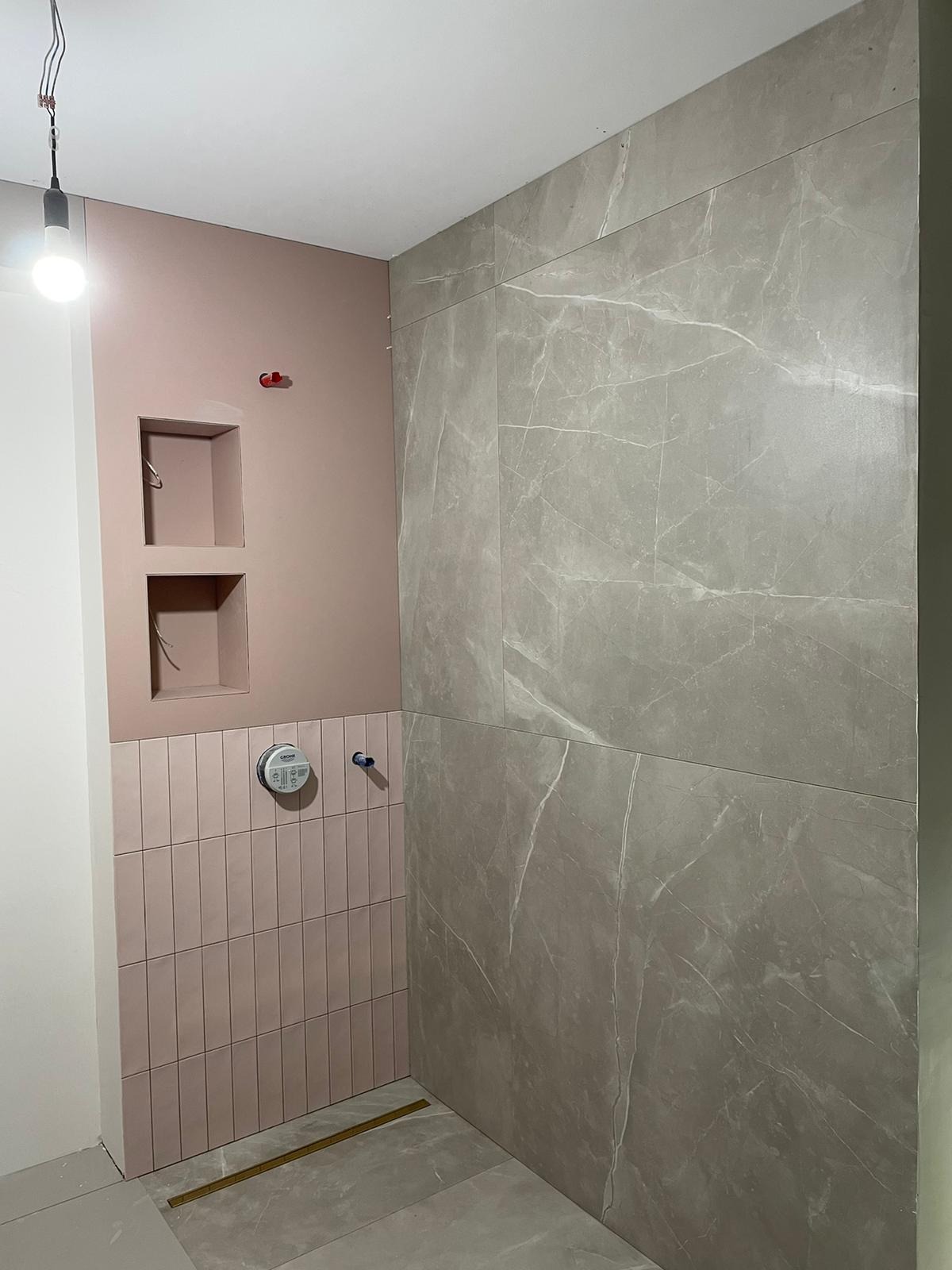 Łazienka w trakcie wykańczania z różowymi i szarymi płytkami, widoczne wnęki ścienne i podtynkowa bateria Grohe.