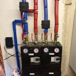 Krystyna Rzedzicka Aquadom - Dwa czarne, kompaktowe moduły AFRISO z manometrami, połączone rurami w izolacji (czerwona i niebieska), sterowane urządzeniami ENGO. Instalacja w pomieszczeniu.