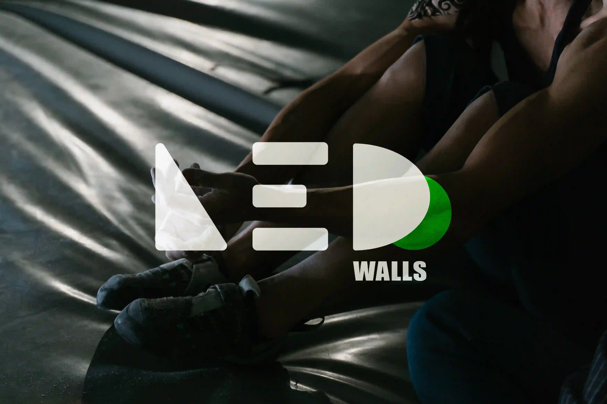 Logo firmy LED Walls na tle podłoża do wspinaczki z widocznymi dłońmi i stopami wspinaczy.