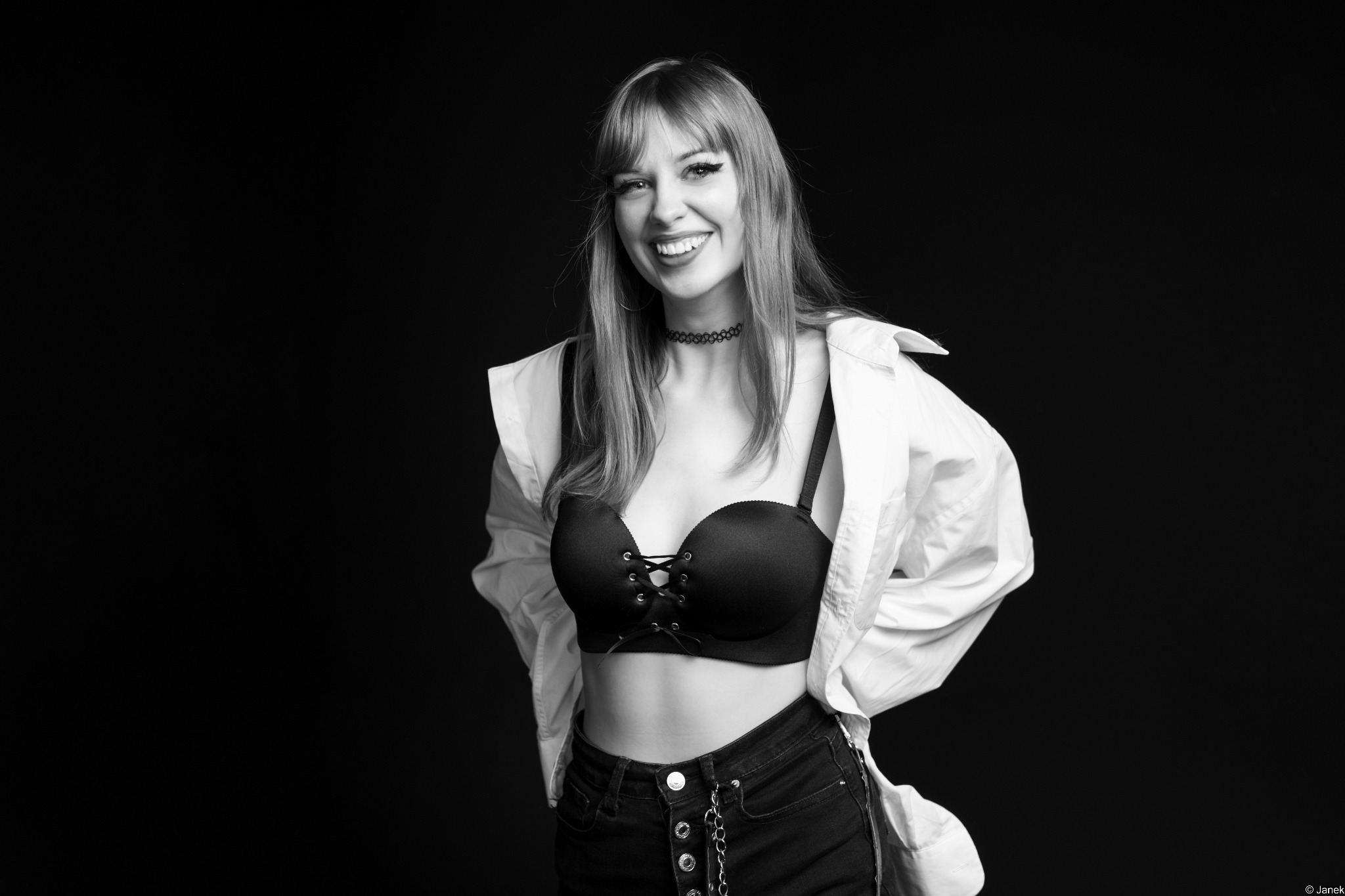 Portret uśmiechniętej kobiety w bieliźnie i rozpiętej koszuli na czarnym tle, wykonany w Warszawie. Uwagę zwraca choker na szyi i mocny makijaż oczu.