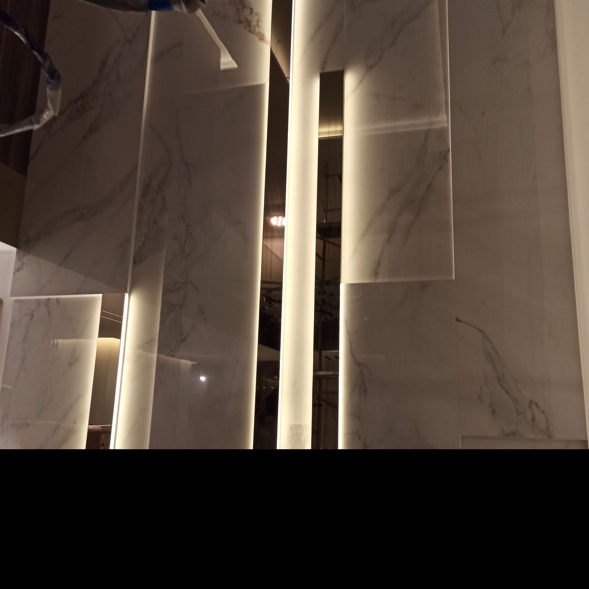 Ściana z płyt marmurowych z podświetleniem LED w trakcie montażu, widoczne zabezpieczenia instalacyjne.