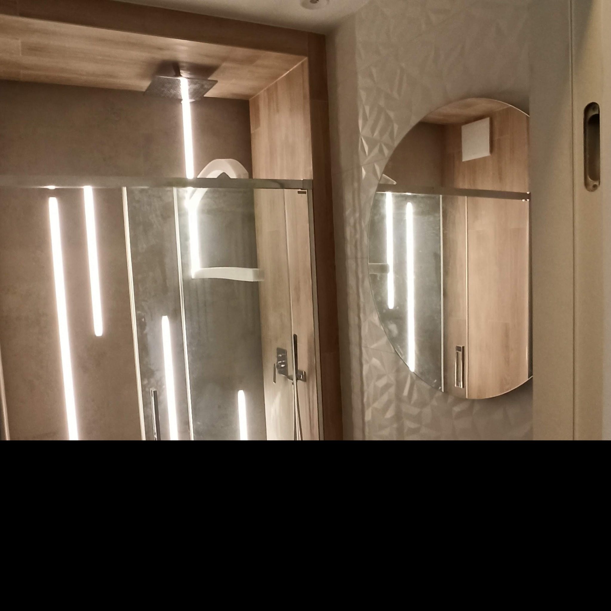 Nowoczesna kabina prysznicowa z podświetleniem LED i okrągłym lustrem w łazience w Warszawie, widoczna w odbiciu szafka.