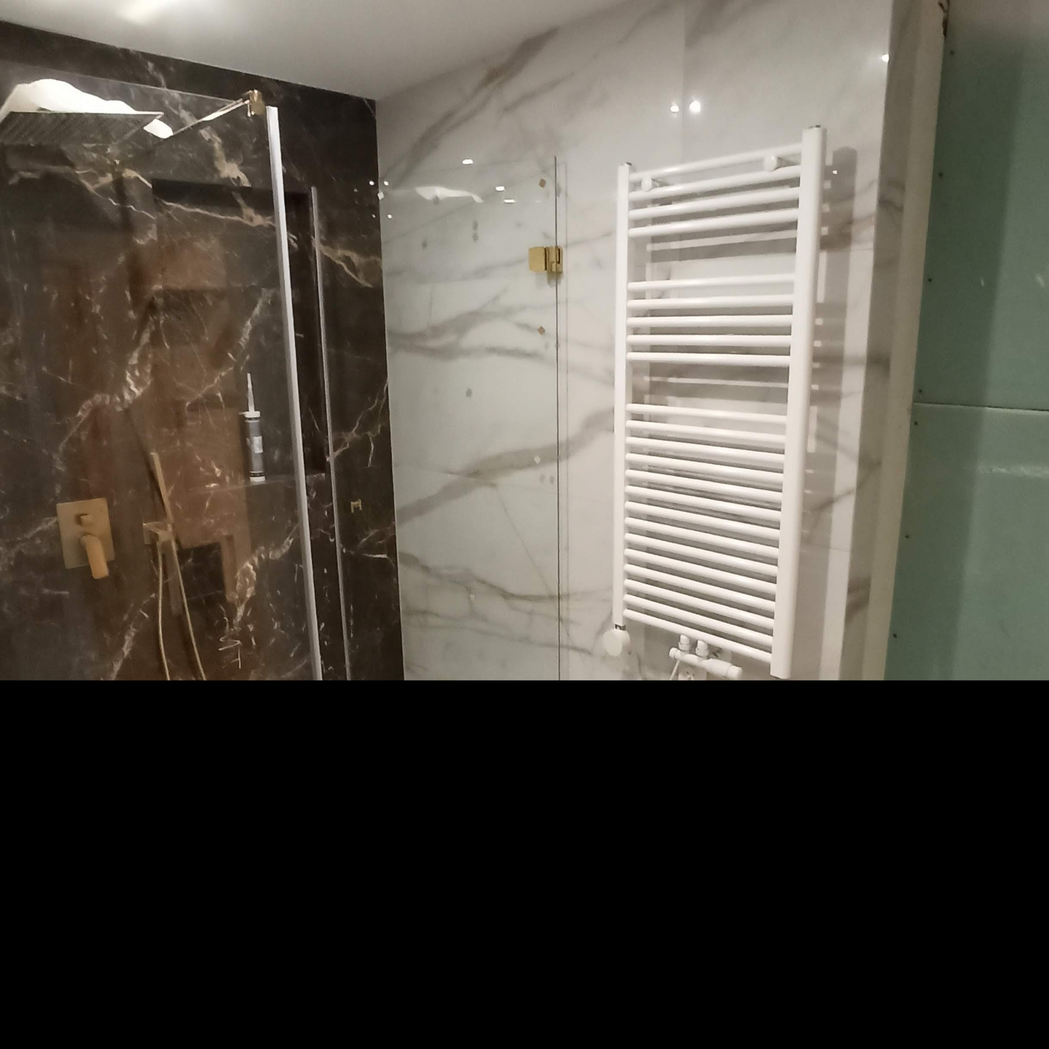 Nowoczesna łazienka z kabiną prysznicową typu walk-in z marmurowym wzorem, grzejnikiem drabinkowym i ścianą przygotowaną pod płytki.