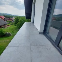 Paweł Mierzwa - Wyłożony szarymi płytkami balkon z widokiem na zielony krajobraz, w tle domy i lasy.