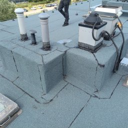 PrimeDach Łukasz Żukowski - Szczegółowe ujęcie płaskiego dachu pokrytego papą z kominami, wentylacją i elementami instalacji, z widocznymi łączeniami i teksturą powierzchni.