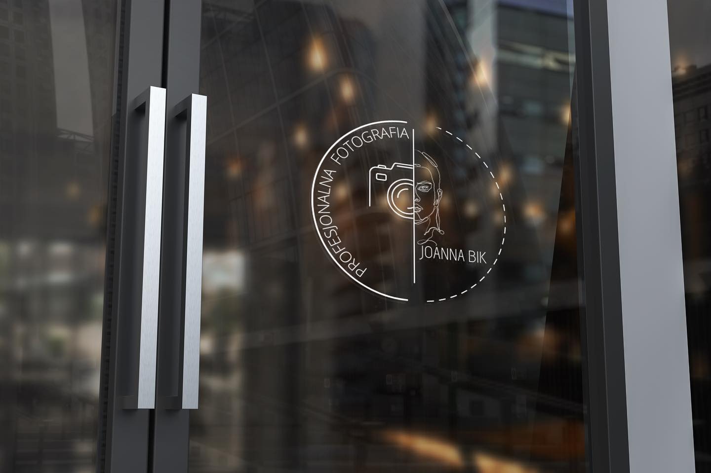 Grafika z minimalistycznym logo fotografa Joanny Bik, naklejona na szklane drzwi wejściowe do biura, widoczne srebrne uchwyty i odbicie miejskiego krajobrazu.