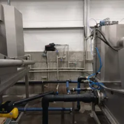 Instalacja przemysłowa z rurami, pompami i elementami metalowymi w hali produkcyjnej, widok z dołu na skomplikowany system rurociągów.