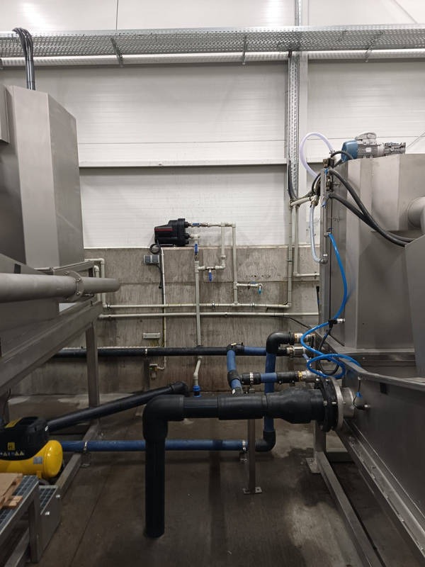 Instalacja przemysłowa z rurami, pompami i elementami metalowymi w hali produkcyjnej, widok z dołu na skomplikowany system rurociągów.