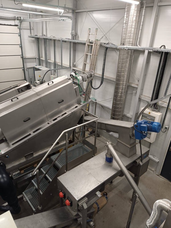 Wnętrze hali z metalową konstrukcją, schodami kratowymi i instalacją przemysłową, widok z góry.