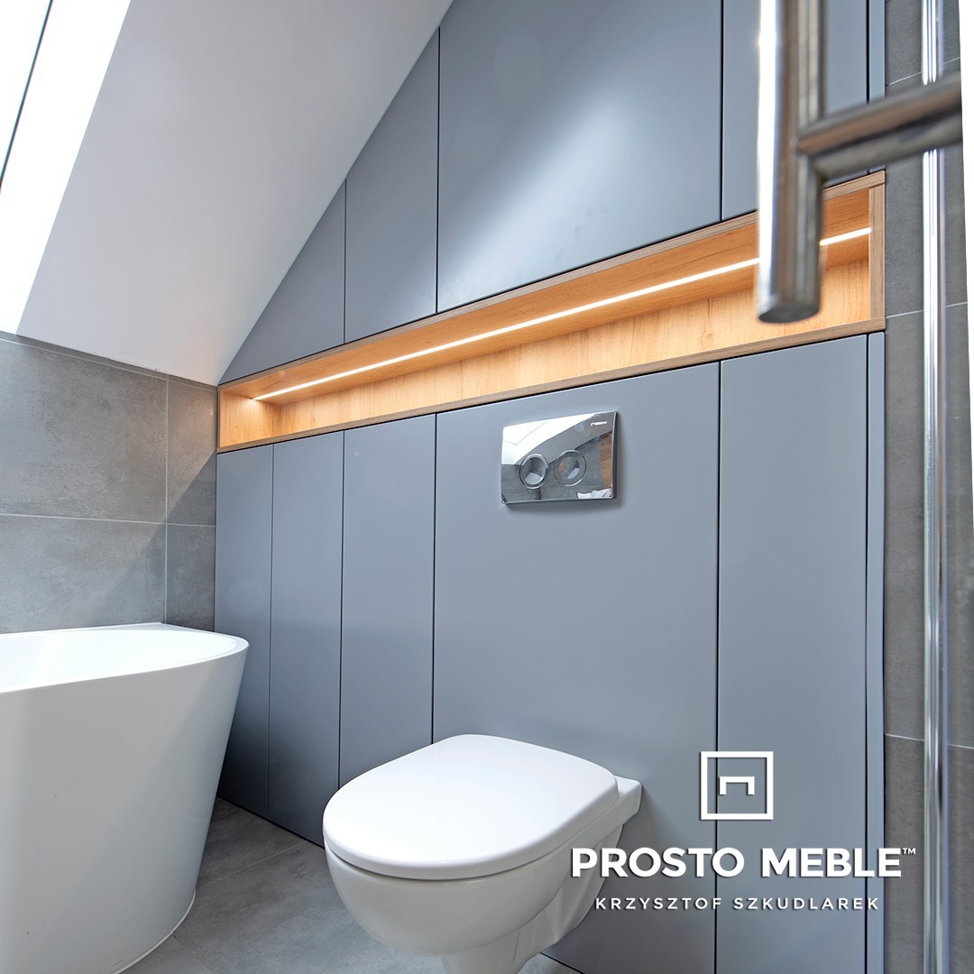 Szara zabudowa meblowa w łazience na poddaszu ze skośnym sufitem, oświetleniem LED i wiszącą toaletą.