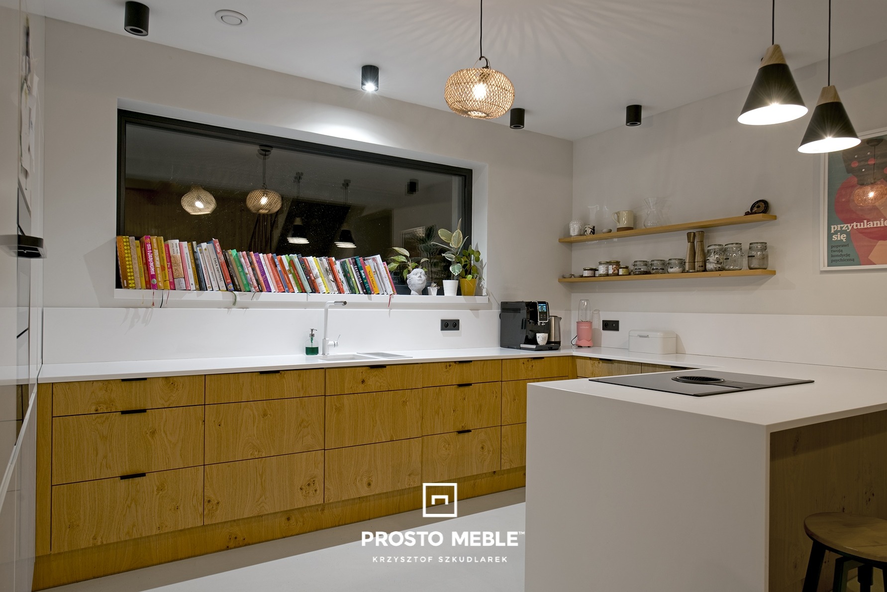 Nowoczesna kuchnia w Poznaniu z drewnianymi szafkami dolnymi i białym blatem, z oknem nad blatem wypełnionym książkami i roślinami, oświetlona wiszącymi lampami.