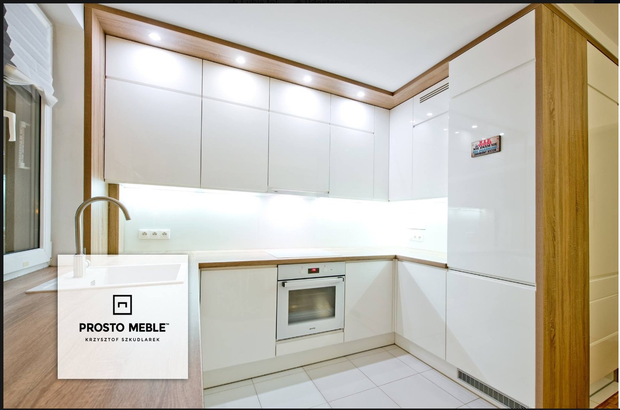 Nowoczesna, jasna kuchnia w kształcie litery L z białymi, lakierowanymi frontami i blatem imitującym drewno. Na lodówce widoczna zabawna tabliczka z napisem.