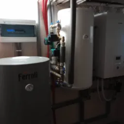 Kotłownia z szarym zbiornikiem Ferroli, białym zbiornikiem i białym kotłem Panasonic na tle ściany z instalacjami, widoczna skrzynka elektryczna.