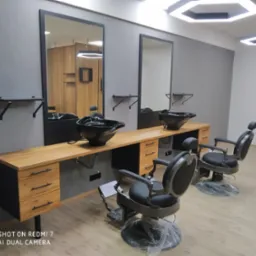 Nowoczesne stanowiska fryzjerskie z drewnianymi blatami, czarnymi umywalkami i lustrami, oświetlone sześciokątnymi lampami.