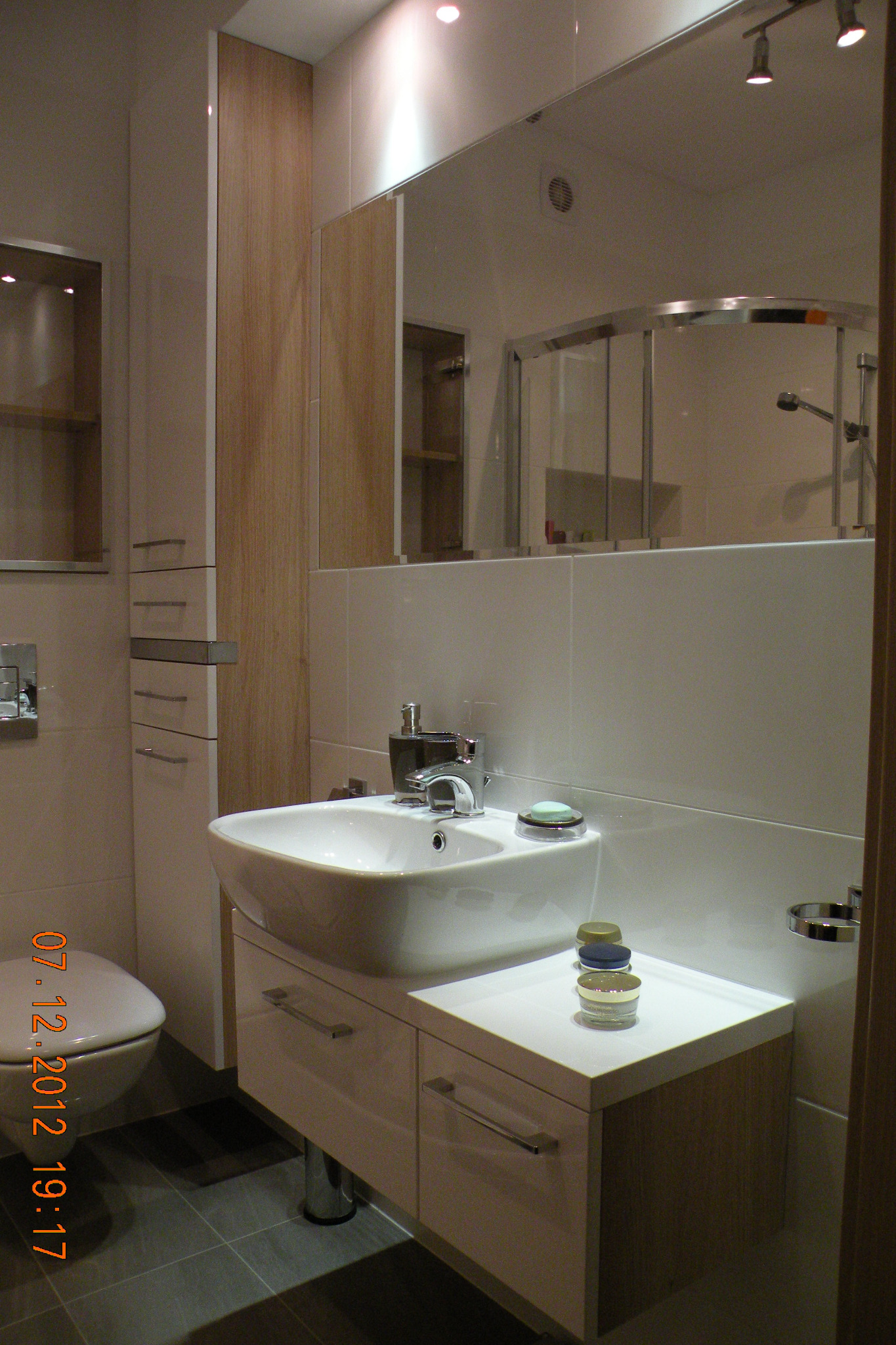 Nowoczesna łazienka z białą umywalką nablatową na szafce z szufladami, wysoką szafką z półkami i lustrem odbijającym kabinę prysznicową.