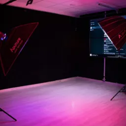 Pusta przestrzeń studia oświetlona lampami Aputure z softboxami, na ścianie widoczny duży ekran z listą odtwarzania muzyki.