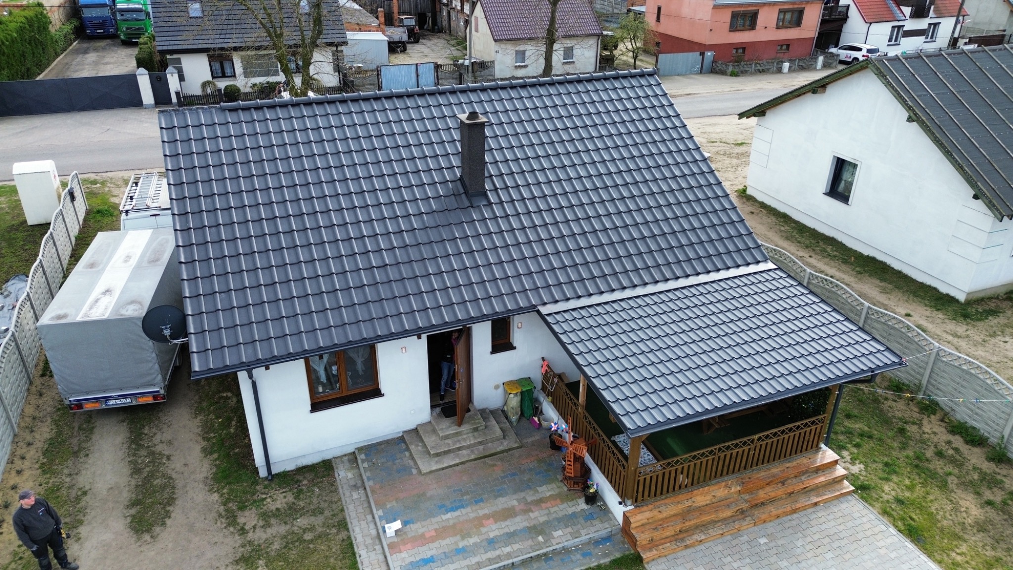 Dom jednorodzinny z nowym, grafitowym pokryciem dachowym w Jarocinie, widok z góry. Na podwórku stoi przyczepa z anteną satelitarną.