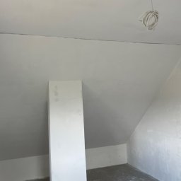 Usługi Budowlane Marek Łukojć - Poddasze w trakcie prac wykończeniowych, widoczna surowa ściana ze śladami szpachlowania, instalacja elektryczna zwisająca z sufitu i instalacja wodna w ścianie.