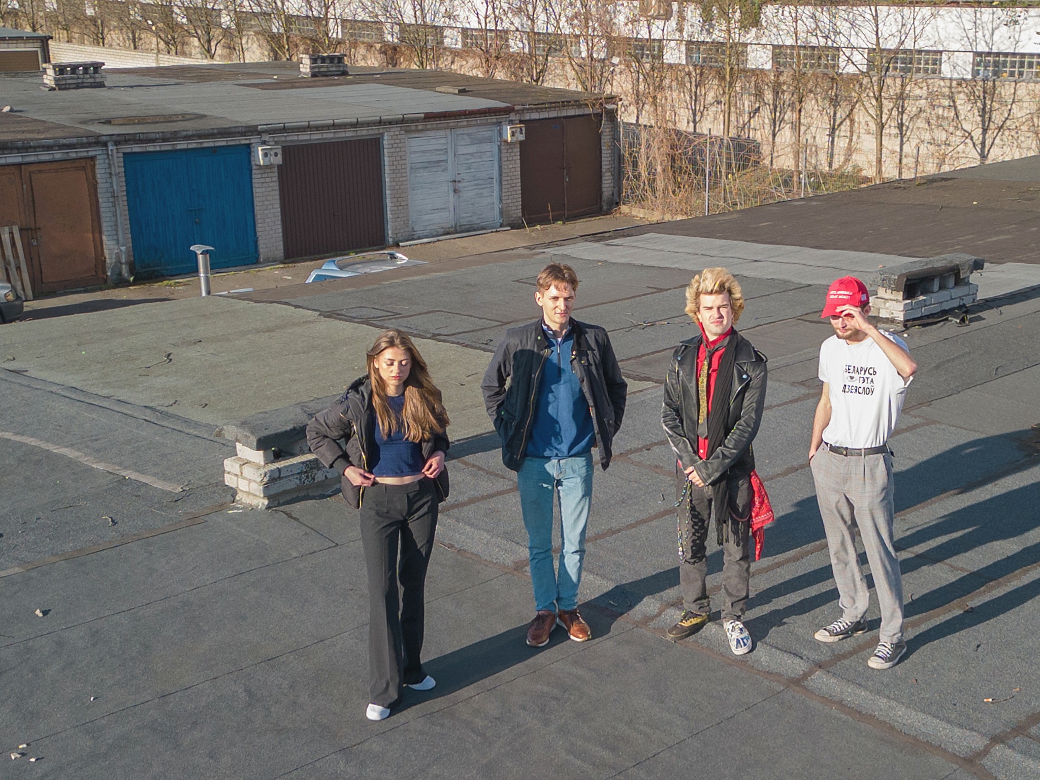 Zespół muzyczny składający się z czterech osób stoi na dachu budynku z garażami w tle, wykonując sesję zdjęciową.
