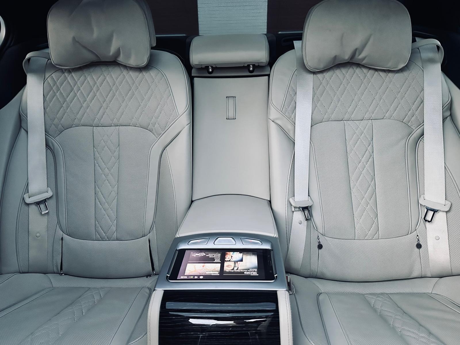 Luksusowe wnętrze samochodu: jasnoszare skórzane fotele z pikowaniem w romby, pasy bezpieczeństwa i dotykowy panel sterowania dla pasażerów z tyłu.