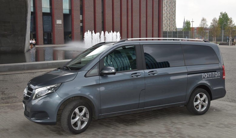 Szary van Mercedes z logo firmy transportowej PORTITOR na tle fontanny i nowoczesnej architektury w Krakowie.