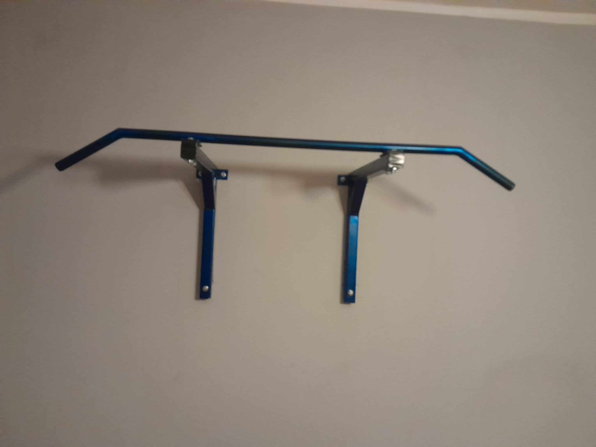 Niebieski, metalowy drążek do podciągania zamontowany na jasnej ścianie, widoczne mocowania.