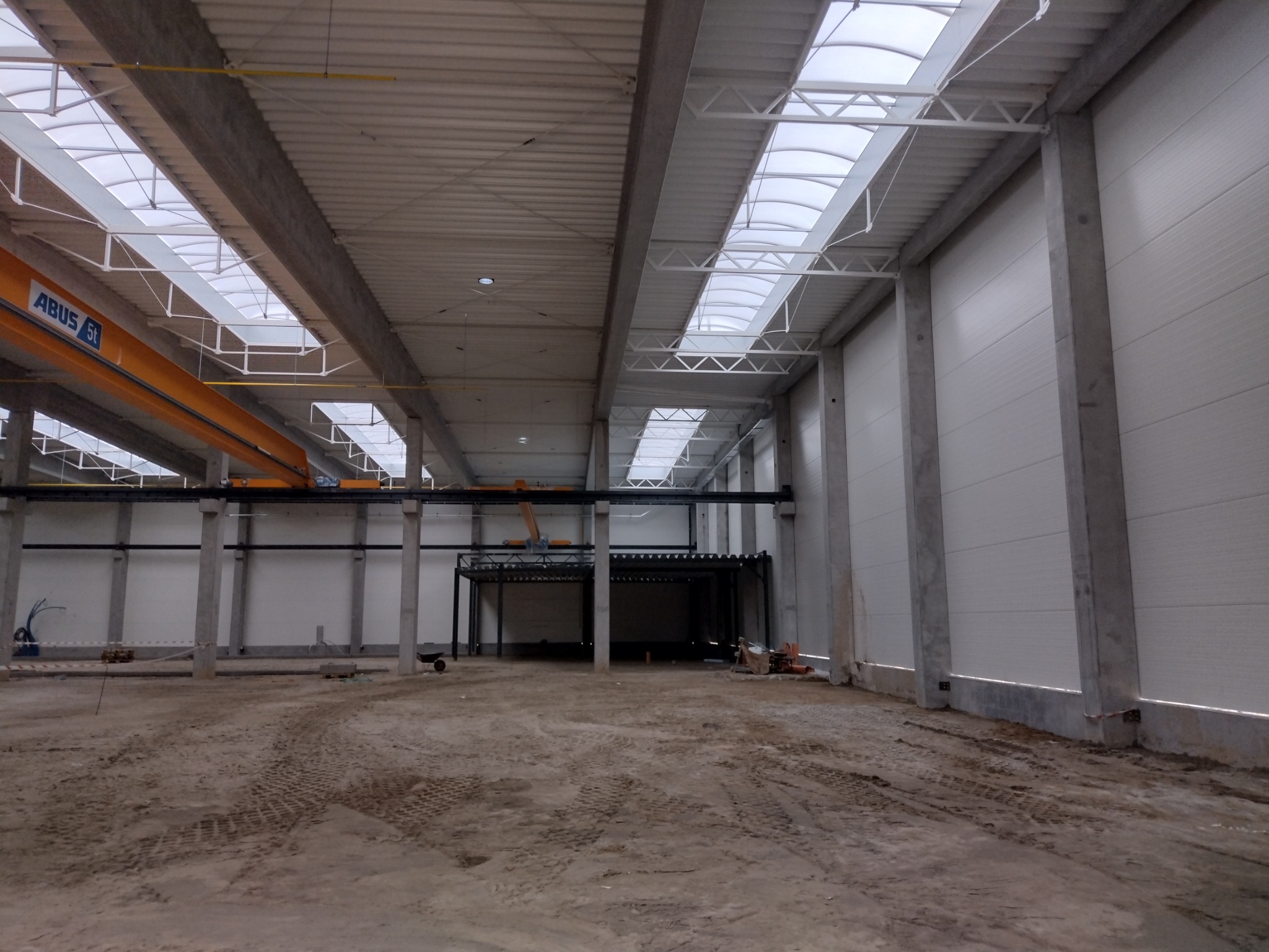 Wnętrze hali produkcyjnej w trakcie budowy z widoczną konstrukcją stalową, suwnicą ABUS i oknami dachowymi.