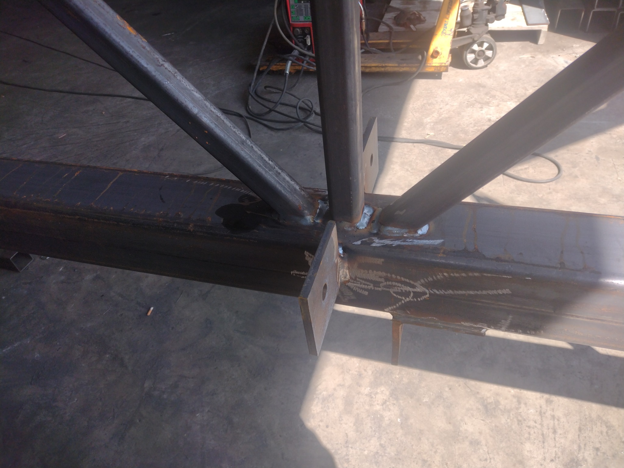 Konstrukcja stalowa z profili spawanych, widoczne spoiny, elementy mocujące i ślady obróbki, w tle sprzęt spawalniczy.