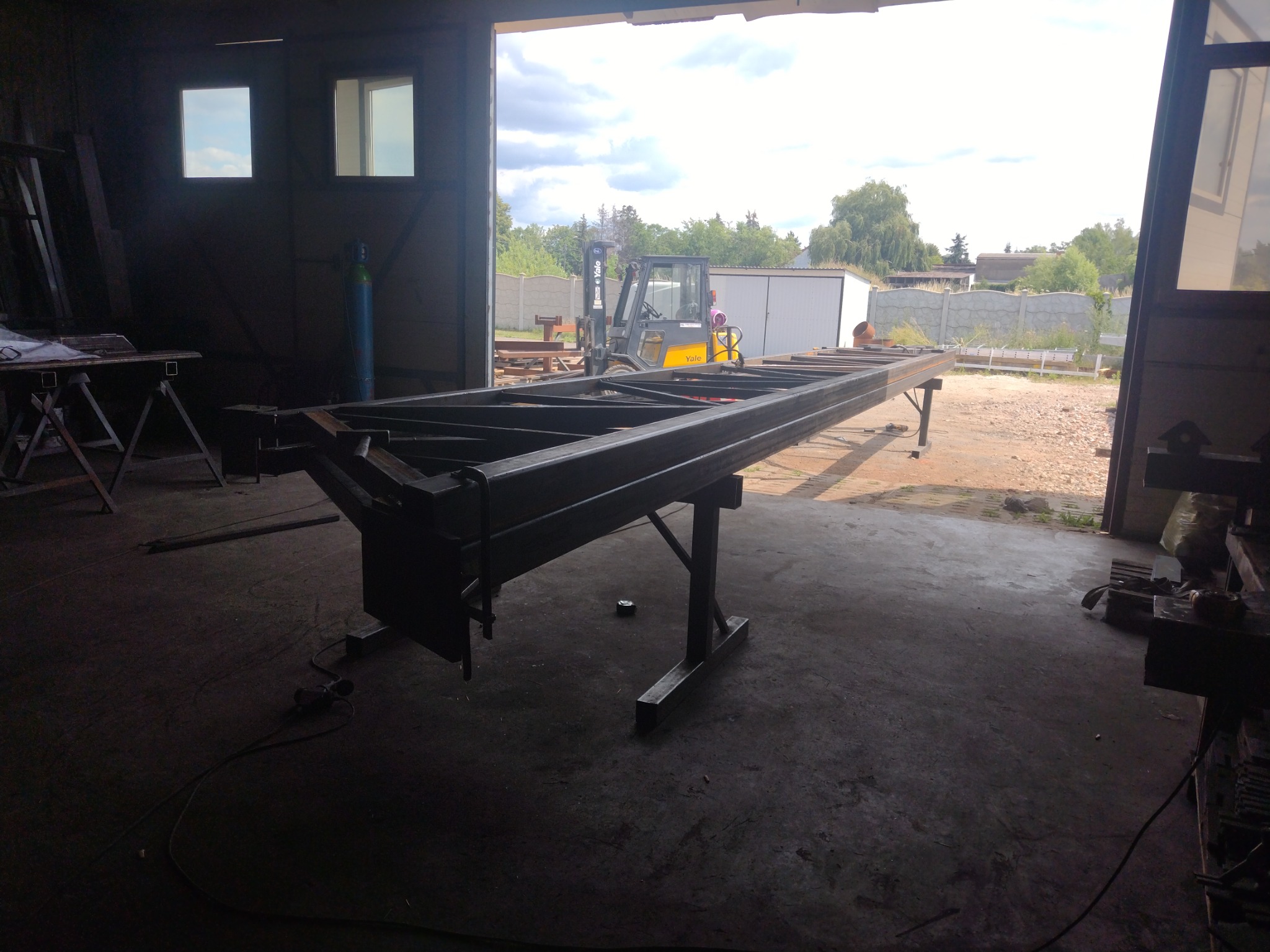 Konstrukcja stalowa ramy, prawdopodobnie pod ogrodzenie lub bramę, na metalowych kozłach w warsztacie, w tle widoczny wózek widłowy.