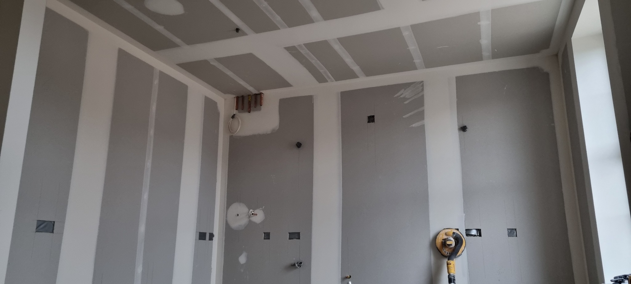 Wnętrze w trakcie wykańczania: ściany z płyt karton gips, z widocznymi instalacjami i otworami pod gniazdka, przygotowane do dalszych prac wykończeniowych, częściowo zaszpachlowane łączenia płyt...