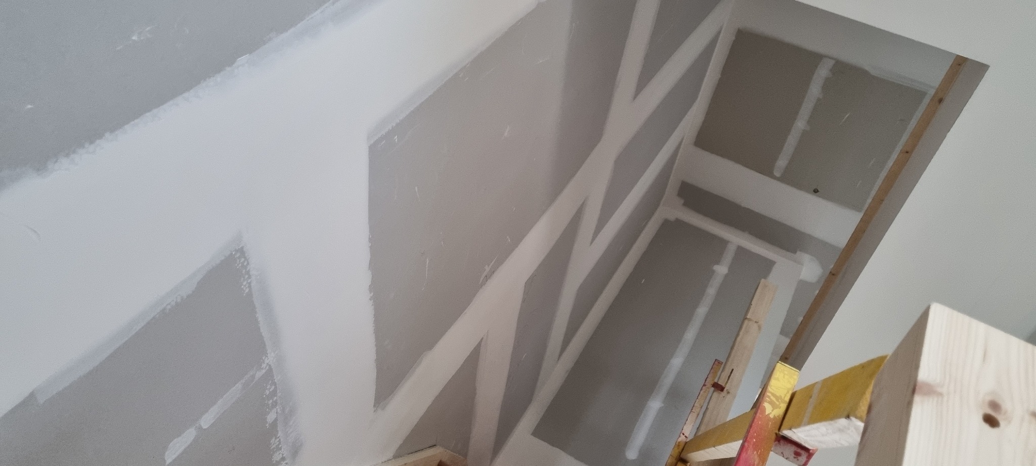 Ściany i sufit w trakcie montażu płyt kartonowo-gipsowych, widoczne profile i częściowo nałożona masa szpachlowa na łączeniach.