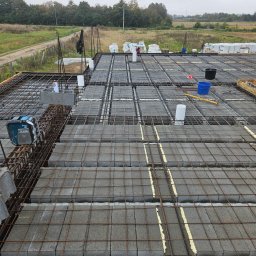 WOJCIECH KROPIDŁOWSKI - Budowa stropu: szalunek zbrojony siatką i bloczkami betonowymi, widoczne narzędzia i materiały budowlane na tle krajobrazu. Etap prac w toku.