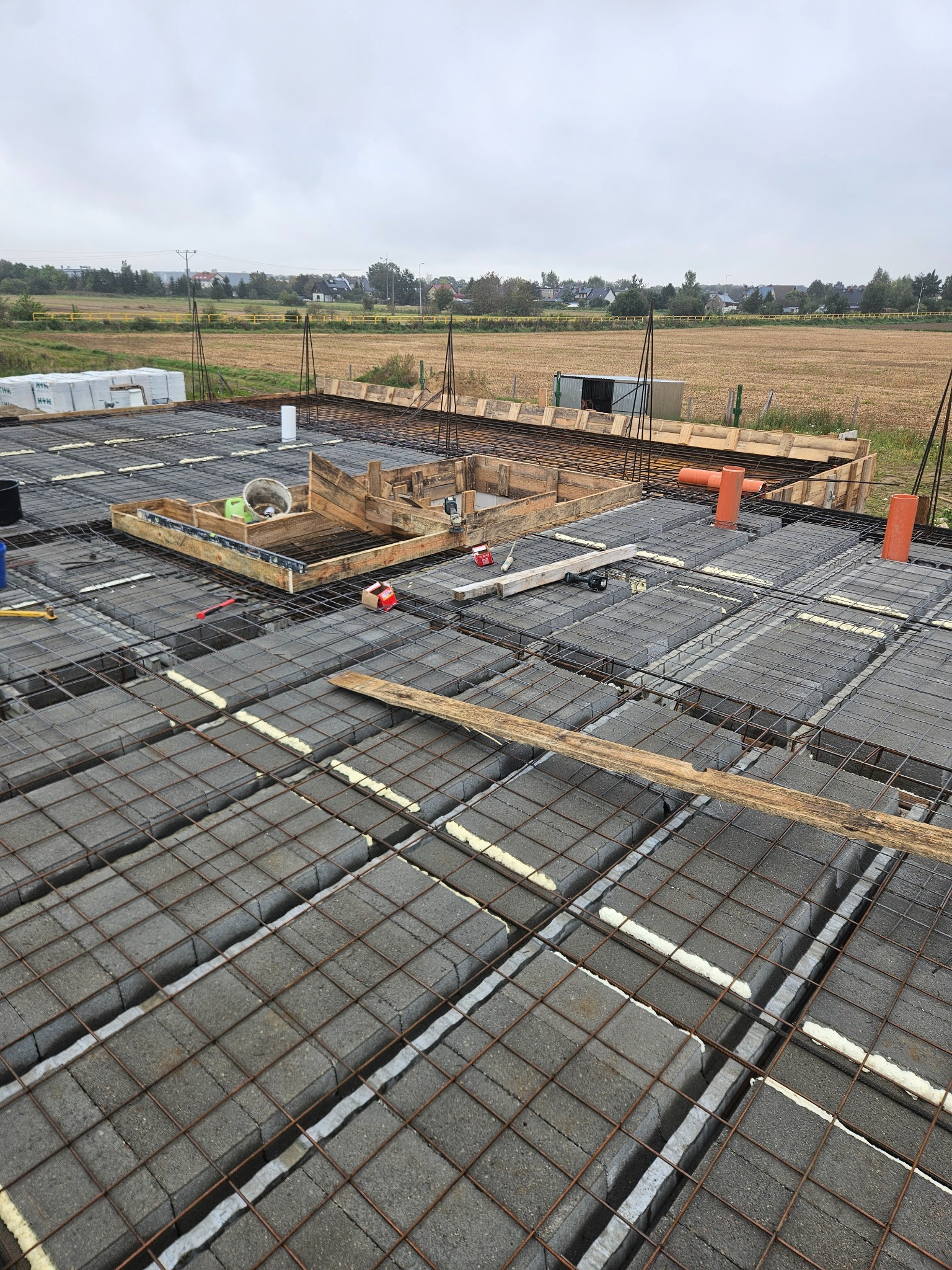 Fundament z bloczków betonowych i zbrojenia, przygotowany do zalania betonem. Widoczne szalunki i narzędzia na tle krajobrazu.