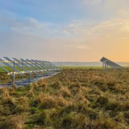Metalowa konstrukcja wsporcza pod panele słoneczne, rozstawiona na zewnątrz na polu, w tle widać wschodzące słońce i lekką mgłę.