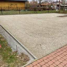 Solid-Tech Lucjan Golonka - Utwardzony teren drobnym kruszywem z betonową obwódką, widoczny fragment chodnika z kostki brukowej, w tle budynek i ogrodzenie z siatki.
