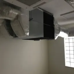 Centrala wentylacyjna z izolowanymi przewodami w obiekcie przemysłowo-biurowym, widok na instalację pod sufitem, kratka wentylacyjna w tle.